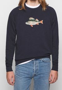 Marinblå sweatshirt med raglanärmar, prydd med en broderad fiskdesign i färgglada detaljer. Tillverkad av ett mjukt material, med ribbade muddar.
