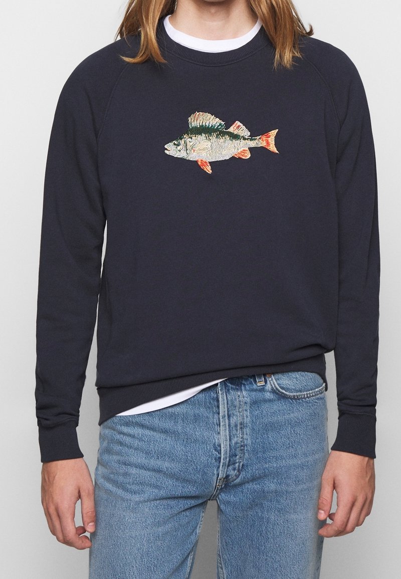 Marinblå sweatshirt med raglanärmar, prydd med en broderad fiskdesign i färgglada detaljer. Tillverkad av ett mjukt material, med ribbade muddar.