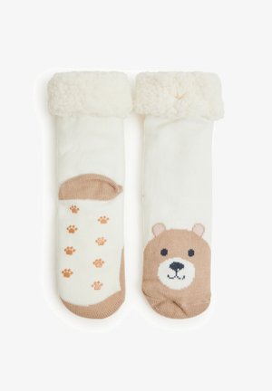 Due calzini crema con soffici polsini bianchi. Uno presenta un design con la faccia di un orso, mentre l'altro ha impronte di zampe in tenui toni di marrone.