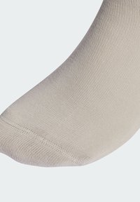 Calcetín beige con una textura suave y elástica. Presenta detalles reforzados en la puntera y el talón, con una parte superior acanalada para un ajuste seguro.