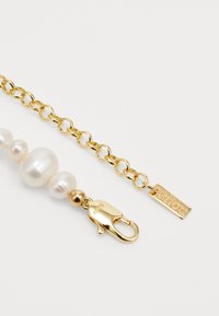 Collana in oro con perle bianche irregolari, dotata di una chiusura a moschettone e di una piccola targhetta incisa con "élieou". Texture liscia e finitura lucida.