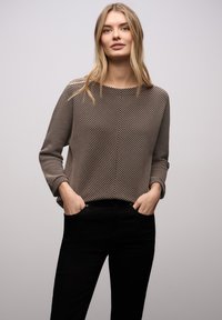 Bluzka z długim rękawem w brązowo-kremowy paskowany wzór, okrągły dekolt, luźny krój, zestawiona z czarnymi spodniami, lekka tkanina, gładka faktura.