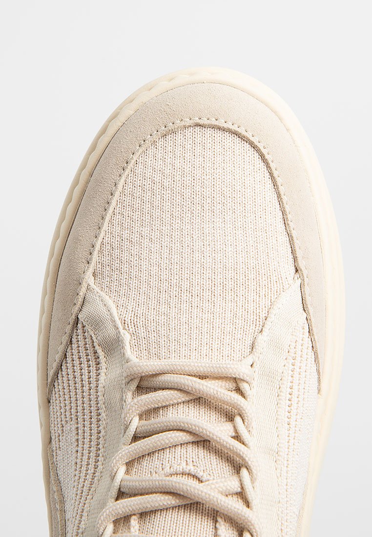 Beige Sneaker mit texturiertem Obermaterial, Wildlederelementen und einer gepolsterten Sohle. Verfügt über aufwendige Nähte und flache Schnürsenkel.