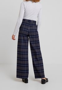 Marineblauwe geruite high-waisted broek met wijde pijpen, voorzien van een riemlus en subtiele plooi-details aan de achterkant. Soepele stoftextuur.