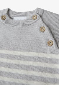 Suéter de punto gris con franjas horizontales color crema, cuello acanalado y tres botones de madera en el hombro para el cierre.