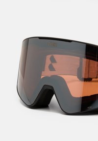Skibrille mit schwarzem Rahmen und großen, orangefarbenen Gläsern. Verfügt über einen Gummi-Rand an der Innenseite für Komfort und Stabilität.