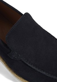 Mocassins en daim bleu marine avec un bout arrondi, des détails cousus et une semelle en caoutchouc de couleur claire. Texture douce et design minimaliste.