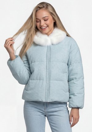 Junge Frau trägt eine hellblaue gesteppte Jacke mit weißem Kunstpelzkragen, lächelt und hält eine Strähne ihres blonden Haares.