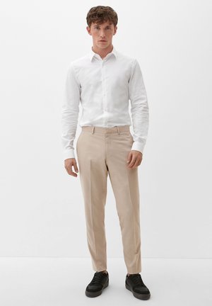 Witte overhemd met lange mouwen, gecombineerd met beige broek en zwarte sneakers. Het overhemd heeft een effen textuur en de broek is op maat gemaakt.