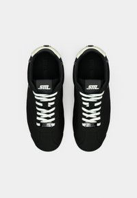 Μαύρα αθλητικά παπούτσια με λείο πάνω μέρος από ύφασμα, λευκά κορδόνια και στρογγυλεμένη μύτη. Ασημένιες λεπτομέρειες στη φτέρνα και το λογότυπο στη γλώσσα.