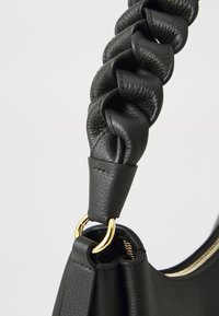 Black leather handbag close-up, featuring a braided strap, gold-tone hardware, textured finish, and a zippered opening.