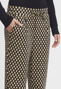 Pantalones a cuadros en negro y dorado con cintura elástica y cordón. Presenta bolsillos a cada lado y una tela suave y texturizada.