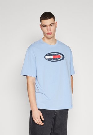 Camiseta de algodón azul claro con un logotipo redondo que incluye el texto "TOMMY JEANS", corte relajado, mangas cortas y cuello de tripulación.