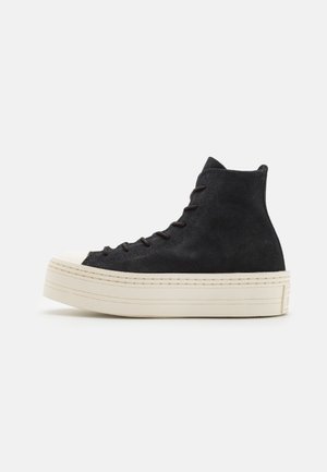 Czarny sneaker typu high-top z grubą białą podeszwą platformową i czarnymi sznurowadłami, pokazany z profilu na jednolitym białym tle.