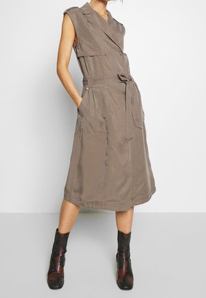 Ærmeløs taupe midi-kjole med bælte, revers og store forlommer, båret med sort-røde mønstrede midtcalsstøvler.