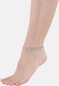 Pulsera de tobillo de plata con un diseño de cadena y acentos de cuentas coloridas, con un símbolo de infinito, llevada en un pie humano.