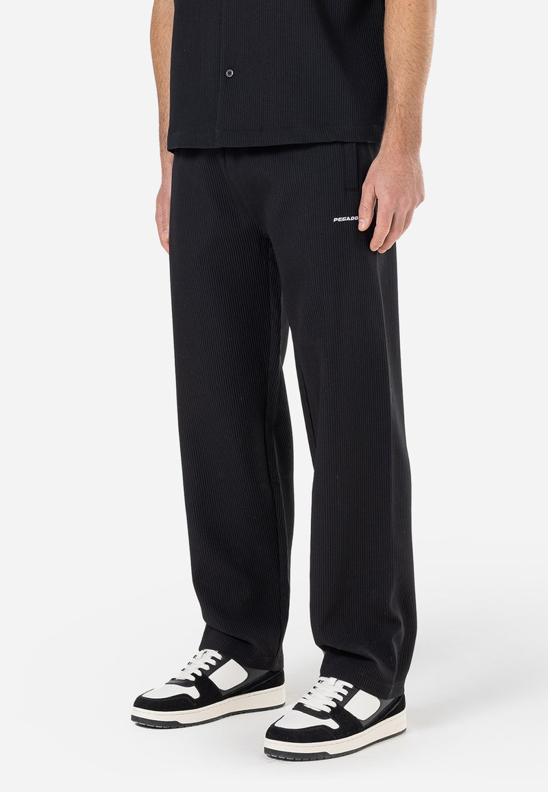 Sorte ribbede bukser har en afslappet pasform, et lille hvidt logo på hoften og er kombineret med sort-hvide sneakers med en tekstureret sål.
