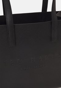 Black synthetic tote bag with textured surface, embossed "TED BAKER LONDON" logo, and dual handles for easy carrying.