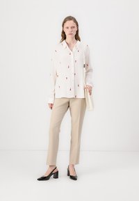 White blouse with red floral embroidery, long sleeves, paired with beige slacks, and black patent heels. Includes a light handbag.