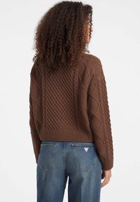 Bruine gebreide trui met een gestructureerd patroon met kabel- en ribbelontwerpen, verkorte lengte, gecombineerd met blauwe denim.