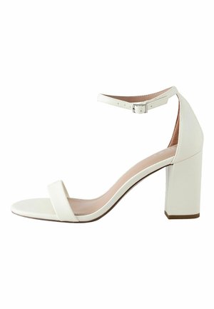 White high-heeled sandal with ankle strap and buckle, open toe, and block heel.