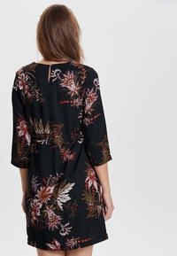 Musta mekko kukkakuviolla punaisen, valkoisen ja vihreän sävyissä. Sisältää kolmanneksen pituiset hihat ja pienen avauksen selässä.
