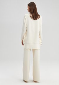 Cream-colored loungewear set featuring a long, slouchy top with side ruching and wide-leg pants. Soft fabric with minimal detailing.