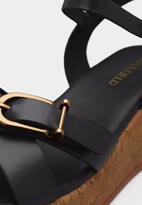 Μαύρο δερμάτινο πλατφόρμα σανδάλι με χρυσή αγκράφα και πάτο με μοτίβο φελλού.