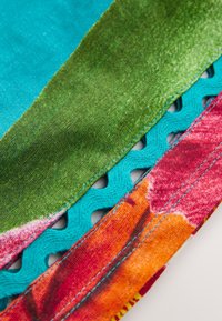 Material colorat cu un amestec de secțiuni turcoaz, verde, roz și portocaliu. Prezintă broderii texturate și detalii decorative decupate.