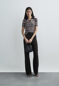 Knitted short-sleeve polo shirt in multicolor pattern, paired with black textured wide-leg pants, holding a small black handbag.