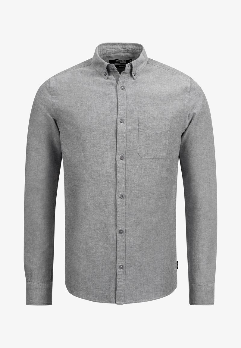 Chemise grise boutonnée en tissu texturé. Manches longues, col, une poche poitrine et patte de boutonnage avant avec boutons foncés.