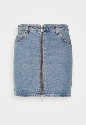 Denim mini-hame, jossa on edessä vetoketju, haalistunut sininen väri ja raaka helma. Yhdistettynä valkoiseen toppiin ja mustiin nauhoilla varustettuihin platform-bootseihin.