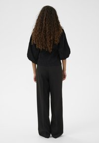 Melns, teksturēts blūze ar pūkainām piedurknēm, pārī ar brīvi pieguļošiem melniem biksēm. Skats parāda apģērba aizmuguri, izceļot siluetu.