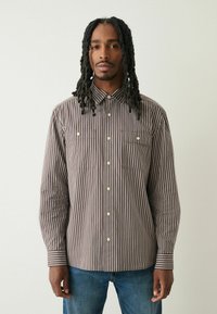 Pasiasta koszula z długim rękawem w kolorze brązowym i kremowym z kołnierzykiem, dwoma kieszeniami na piersi oraz zapięciem na guziki; gładka tkanina; prosty krój.