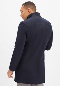Marineblauer Mantel mit taillierter Passform, hohem Kragen und glatter Textur. Verfügt über Nähte und ein sauberes Rückendesign.