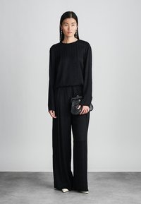 Svart to-delt antrekk med langermet topp og vide bukser. Teksturert stoff, kombinert med en liten svart clutch med krokodillemønster.