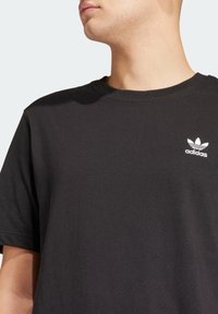 Svart bomull t-shirt med rund hals, med en liten vit Adidas-logotyp på vänster bröst. Mjuk textur och avslappnad passform.
