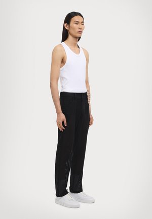 Hvid ærmeløs tanktop, sorte mesh-bukser med åben vævning og hvide sneakers. Minimalistisk design med en afslappet pasform.
