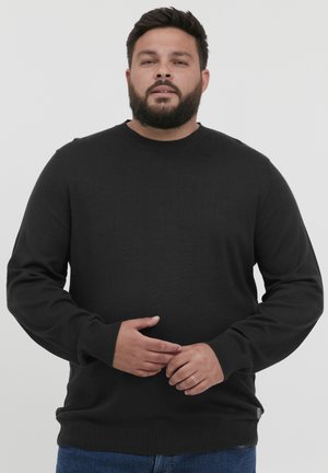 Pull en maille noir avec un col rond et des poignets côtelés. Le tissu semble doux et extensible, avec un léger éclat.