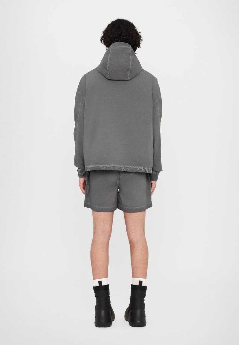 Hoodie grigia con collo alto e pantaloni corti, entrambi in un tessuto morbido. Presenta una vestibilità rilassata e dettagli di cucitura visibili. Stivali neri completano il look.