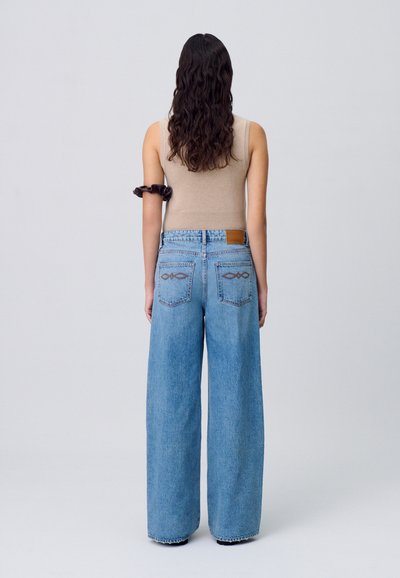 Jeans in denim blu a gamba larga con vita alta, dotati di due tasche posteriori decorate con un motivo cucito. Il tessuto presenta una finitura sbiadita.