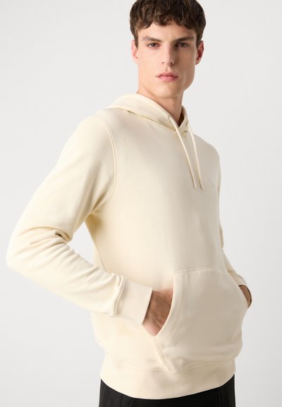 Hoodie de couleur crème en tissu doux, avec une poche avant, une capuche avec cordon de serrage et des poignets côtelés, au design décontracté.