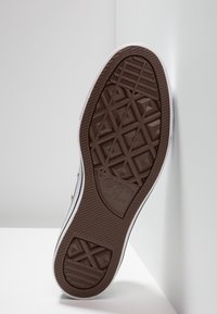 Semelle de chaussure en caoutchouc brun texturé avec un motif étoile, bordée d'un contour blanc, étiquetée "Converse All Star".