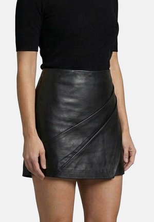 Frau trägt schwarzen Kurzarmtop und schwarzen Leder-Minirock mit diagonaler Naht, auf Oberschenkelmitte gekürzt.