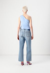 Top azul claro de un solo hombro, diseño ajustado, combinado con jeans de mezclilla azul claro de tiro alto y sandalias de tacón moradas con tiras.