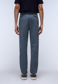 Grå, letvægtsbukser med lige ben, der har to baglommer og minimale stikninger. Bæres med casual sneakers.