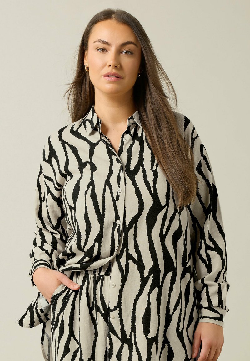 Camisa de botones de manga larga en beige con atrevidas rayas de cebra en negro. Está hecha de una tela suave, con un cuello clásico y mangas con puños.