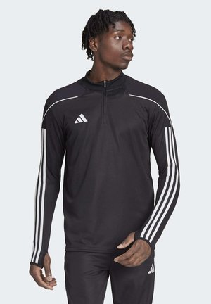 Zwarte sportjas met een kwart-rits, voorzien van witte strepen op de mouwen en een Adidas-logo op de borst. Gelaagde schouderpanelen.