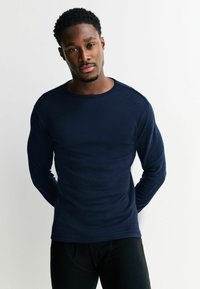 Navy long-sleeve top, crew neck, fitted design with ribbed texture. Paired with black bottoms. Simple and clean construction.