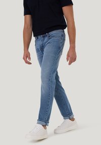 Jeans en denim bleu clair avec une coupe droite, un lavage délavé, un design à cinq poches et des ourlets retroussés, associés à des baskets blanches.